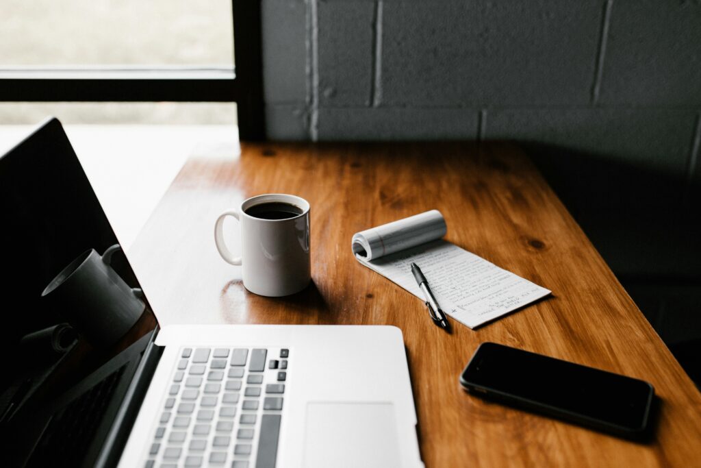 laptop, phone, notepad, and cup of coffee