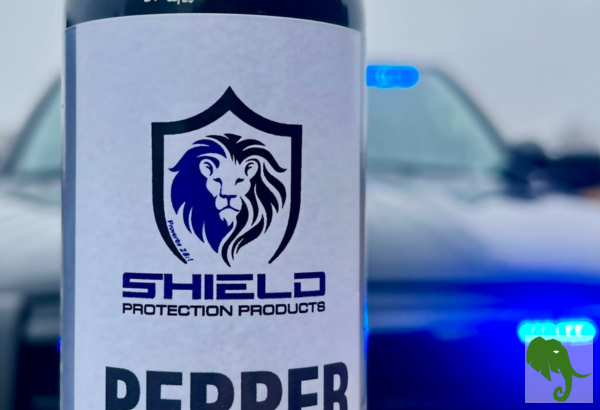 Bottle of Shield Protection Products (affiliate) pepper spray in front of a police patrol car