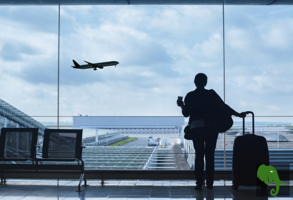 View out airport window with traveler standing and airplane taking off in the background