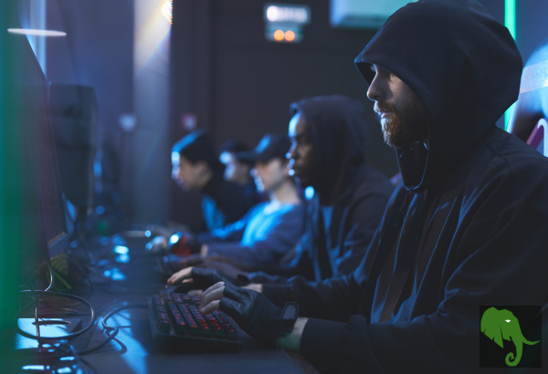 Individuals wearing dark hoodies sitting in front of computers and typing
